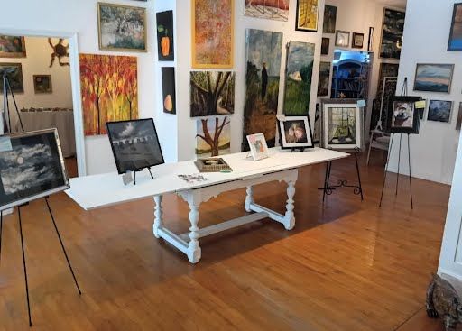 Long white table in the middle of the gallery surrounded by paintings on easels