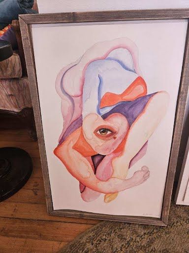 Framed watercolor of an abstract figure with a single eye, in orange, blue and violet